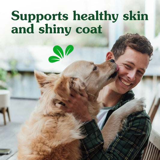 A joyful man smiling as a golden retriever licks his face, with the text "supports healthy skin and shiny coat" and a green leaf icon at the top.